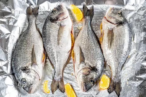 Frische, rohe Dorado-Fische mit Zitronenscheiben auf Alufolie, aus der Sicht von oben
