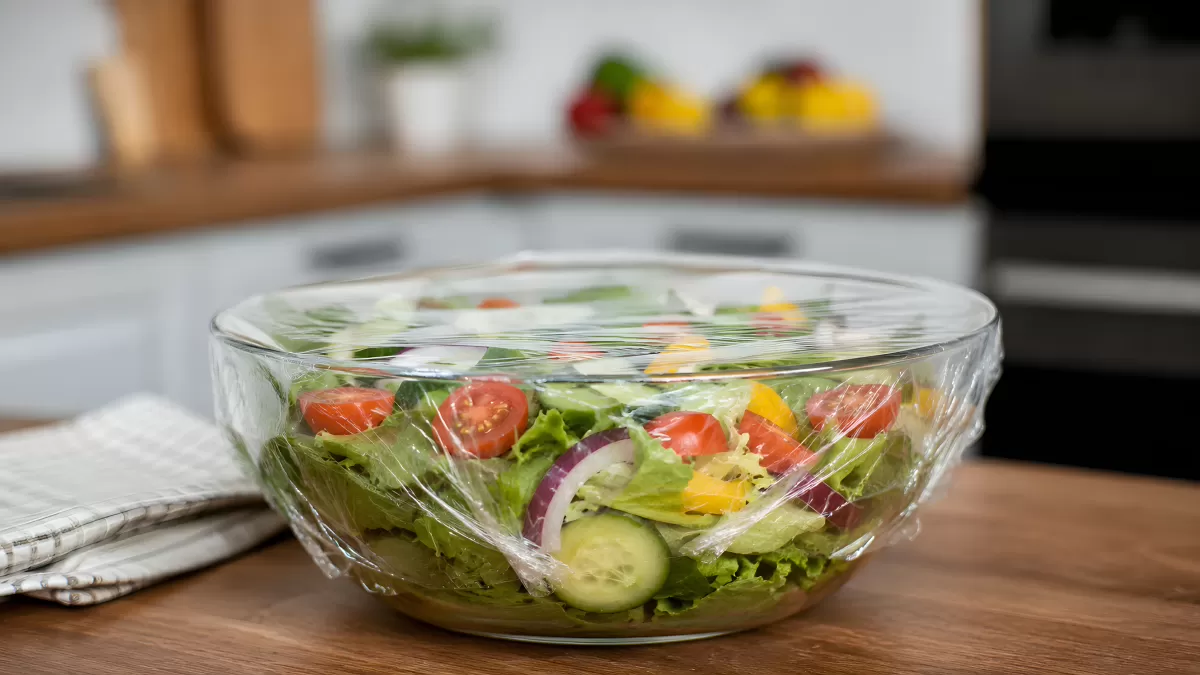 Frischer bunter Salat in Glasschüssel mit Frischhaltefolie