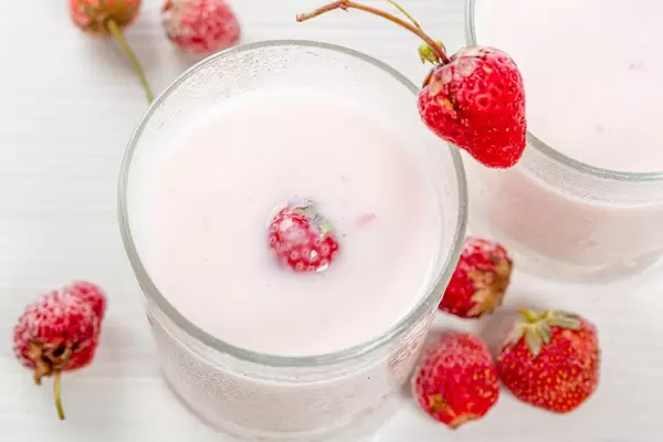 Frischer Erdbeerjoghurt mit reifen Erdbeeren auf einem weißen Tisch