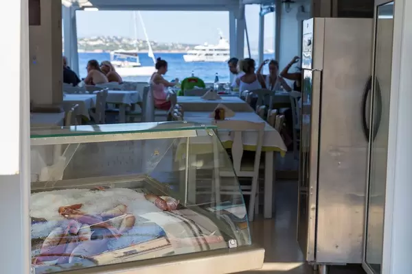 Frischer Fisch auf Eis in einer Kühltruhe, mit Restaurantbesuchern am Fensterplatz mit Meerblick
