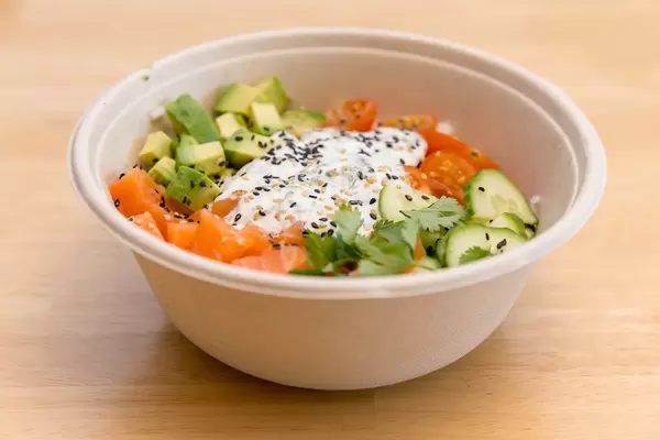 Frischer Lachs mit Avocado und Gemüse wie Gurken und Tomaten in Schüssel auf Holztisch