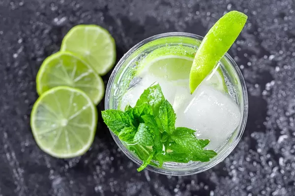 Frischer Mojito mit Eiswürfeln, Minzblättern und Limette, auf einem schwarzen Schieferstein