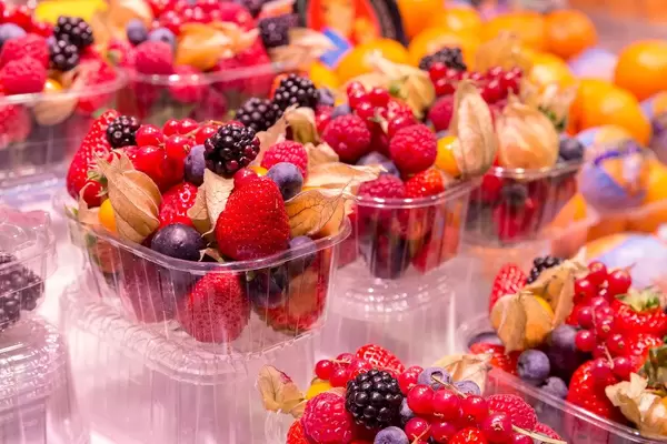 Frischer Obstsalat mit Erdbeeren, Johannisbeeren, Blaubeeren und Brombeeren in Plastikverpackungen, werden in den Markthallen Mercat de la Boquerìa in Barcelona, Spanien, verkauft