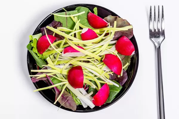 Frischer Salat mit Spinatblättern, Lauch und Radieschen auf einem schwarzen Teller in obene Aufnahme