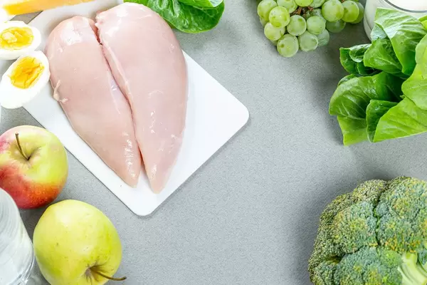Frisches Hähnchenfleisch-Filet, grüne Äpfel und Weintrauben, Salat und Brokkoli auf grauem Hintergrund, aus der Sicht von oben