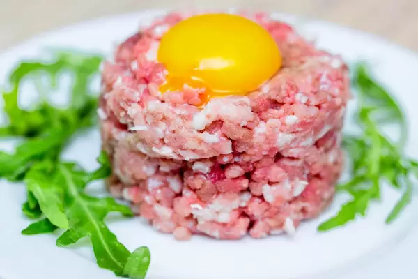 Frisches Rindstatar, angerichtet mit rohem Eigelb und frischen Rucolablättern auf weißem Teller