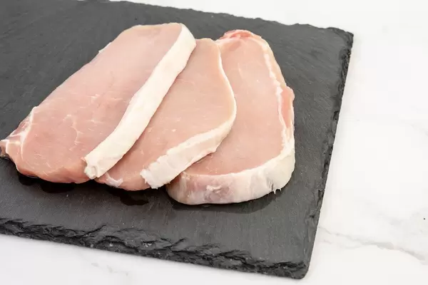 Frisches, rohes Schweinefleisch vom Metzger, auf einer schwarzen Schiefersteinplatte