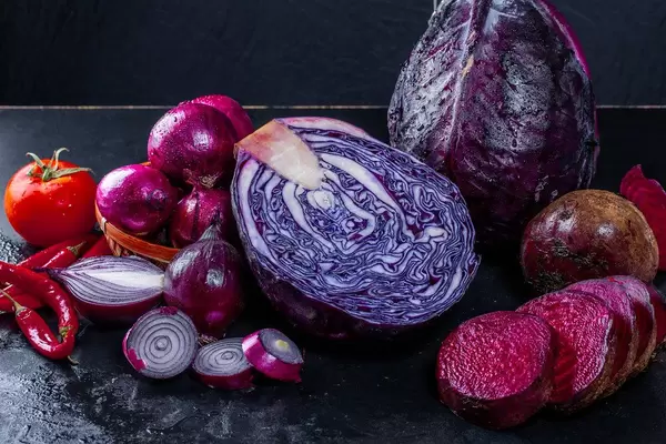 Frishes Gemüse, rote Zwiebeln, Rotkohl, rote Beete, Chili und Tomaten mit Wassertropfen auf schwarzem Untergrund