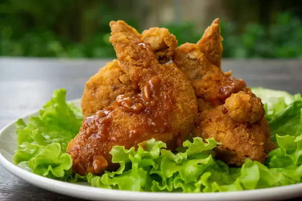 Fritierte Hühnerflügel mit scharfer Tomatensoße auf Salatblättern auf einem Teller Nahaufnahme