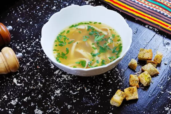 Frittatensuppe in einem weißen Tiefteller und Croutons auf einem schwarzen Tisch