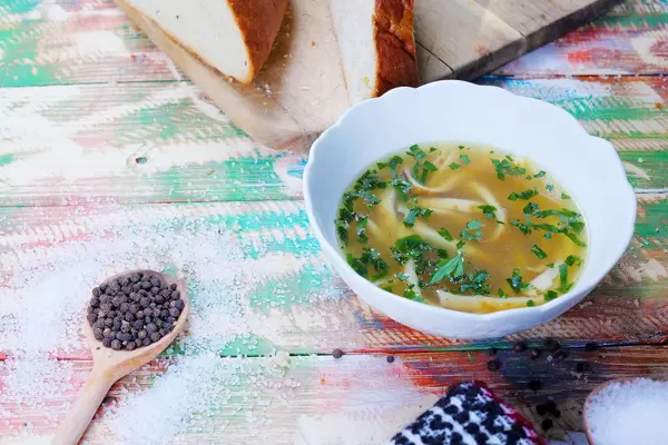 Frittatensuppe: Rindfleischbrühe mit Streifen von Eierkuchen, serviert mit Salz und Pfeffer auf einem bunten Tisch im Vintage-Stil