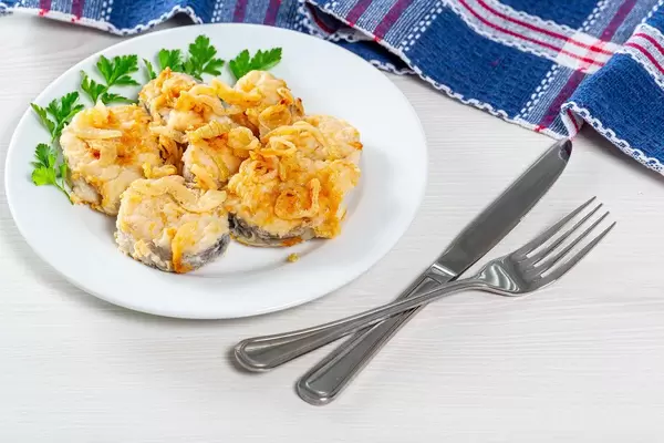 Frittierte Fischstücke mit frischen Zwiebeln und Petersilie,  auf einem weißen Teller