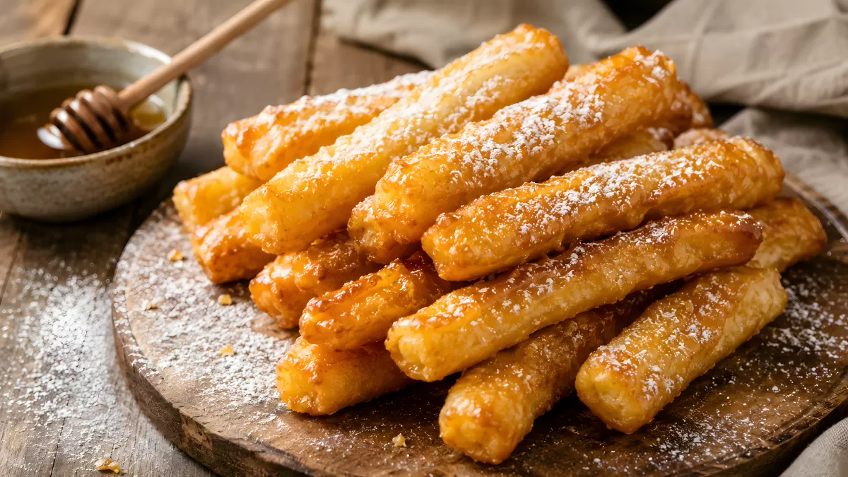 Frittierte Teigstangen mit Puderzucker und Honig
