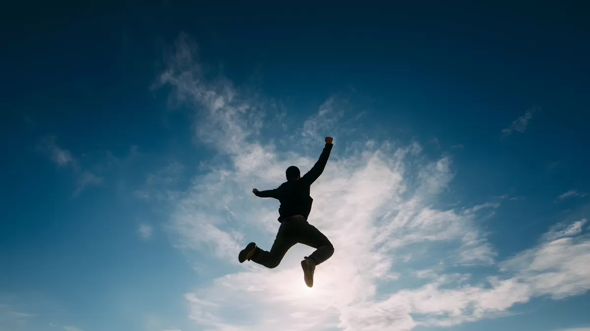 Fröhlich springender Mann vor blauem Himmel