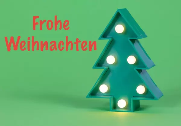 Frohe Weihnachten in roter Schrift auf grünem Hintergrund mit beleuchtetem Weihnachtsbaum
