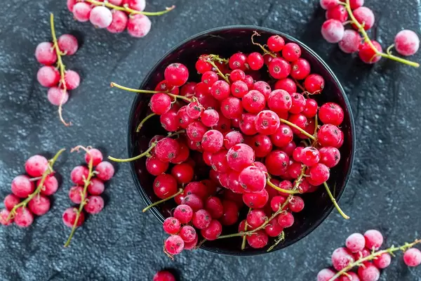 Frozen red currant in a black bowl on a black stone tray. Top view (Flip 2019)