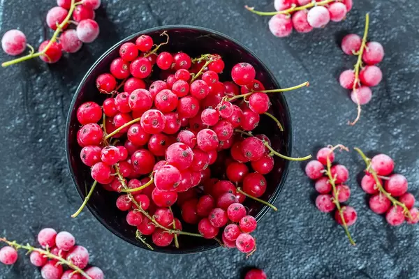 Frozen red currant in a black bowl on a black stone tray. Top view