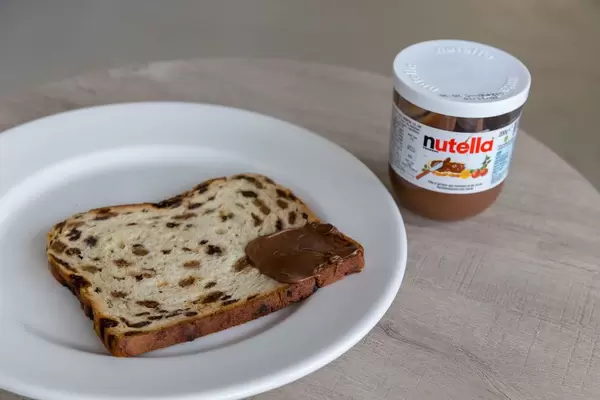 Früchtebrot, an einer Ecke mit Nutella bestrichen auf Teller neben Nutella-Glas
