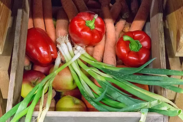 Frühlingszwiebeln, rote Paprika und Karotten in einer Holzkiste