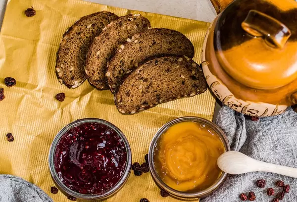 Frühstück aus Scheiben dunklem Brot, Marmelade in Glasschale und Honigtopf