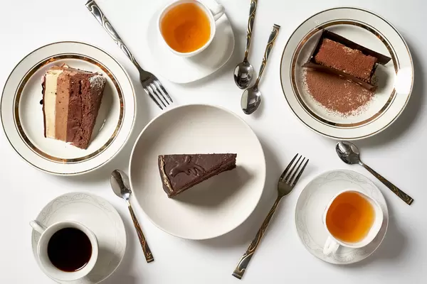 Frühstück für drei: Kaffee- und Teetassen, drei verschiedene Tortenstücke und Besteck