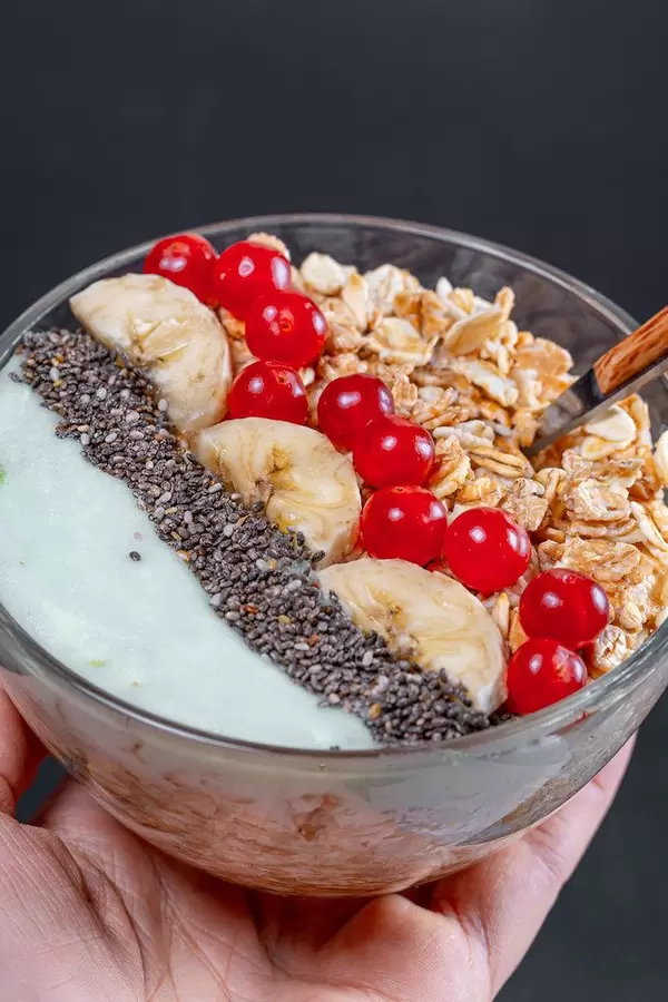 Frühstück mit Haferflocken und Früchten in einer Glasschale in der Hand einer Frau