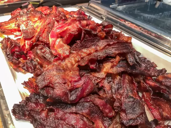 Frühstücksspeck Bacon, geschnitten, auf einem weißen Teller, am Frühstücksbüfett