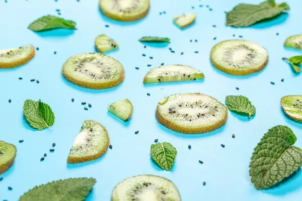 Fruit background with fresh kiwi slices, black sesame seeds and mint leaves on blue
