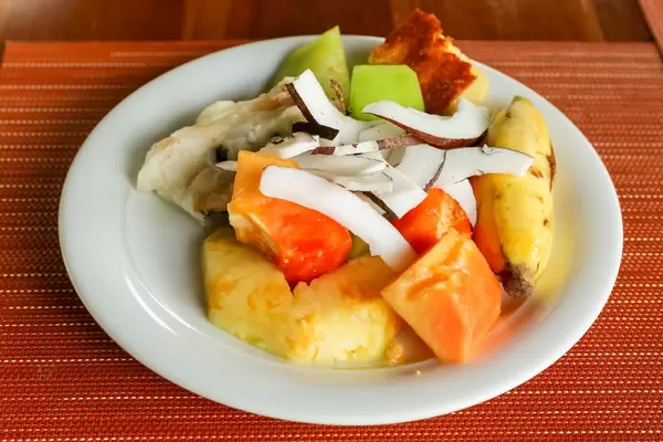 Fruit salad with pineapple, coconut, banana and papaya on white plate