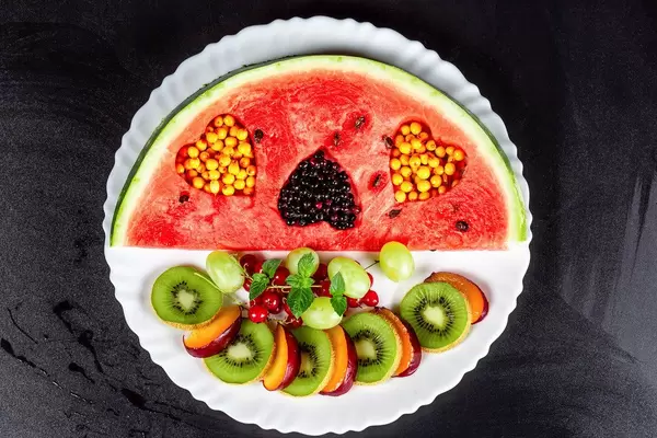 Fruit slicing on a white plate with berries on a black background