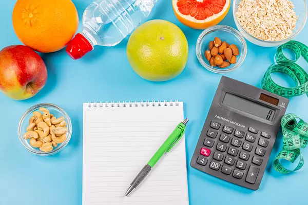 Fruits, oatmeal, nuts, calculator, bottle of water and measuring tape on blue background with notepad and pen