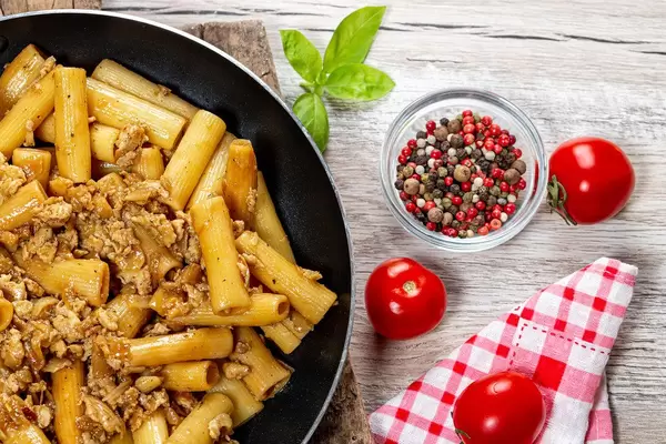 Frying pan with pasta and chicken on a wooden background with spices and fresh tomatoes (Flip 2019)