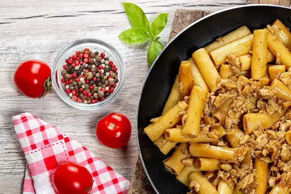 Frying pan with pasta and chicken on a wooden background with spices and fresh tomatoes
