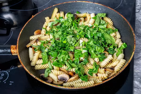Frying pan with pasta, mushrooms and herbs on the electronic hob (Flip 2019)