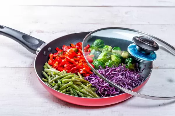 Frying pan with sliced vegetables on white wooden table