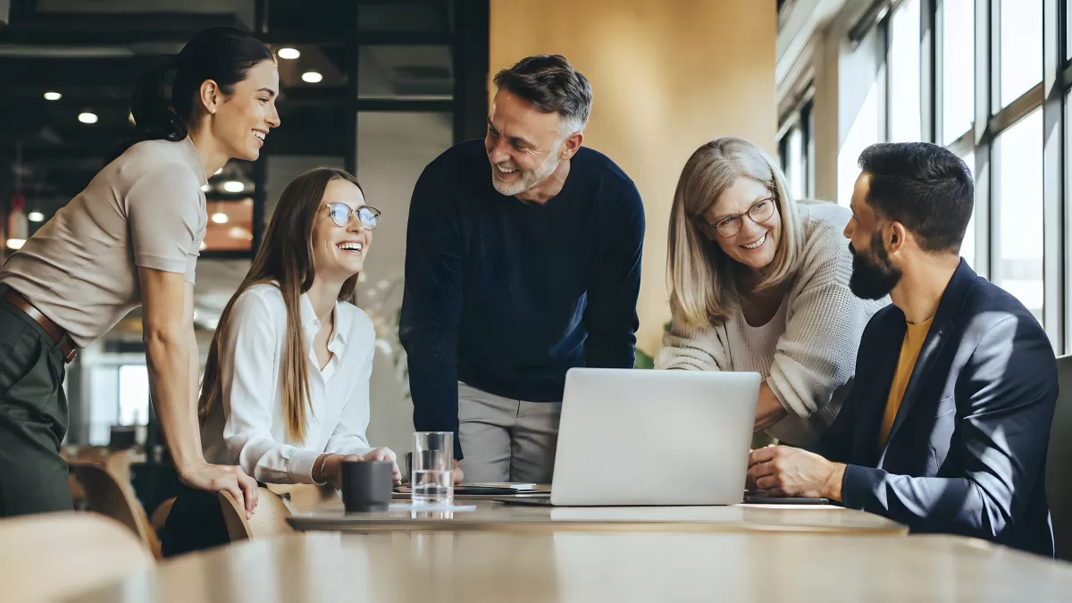 Fünf Kollegen lachen gemeinsam über Laptop im Büro