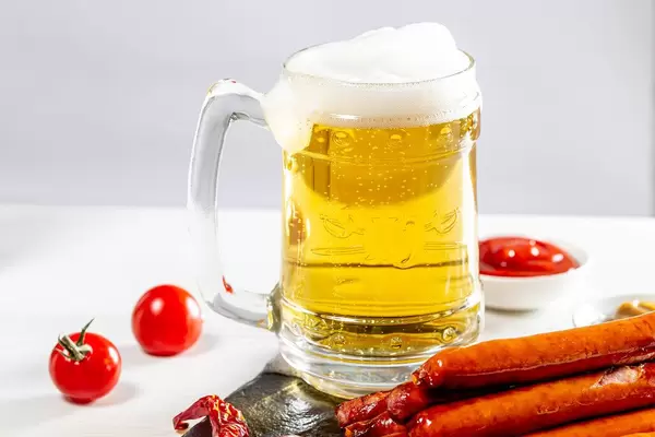 Full glass of light beer with foam and sausages on white table (Flip 2019)