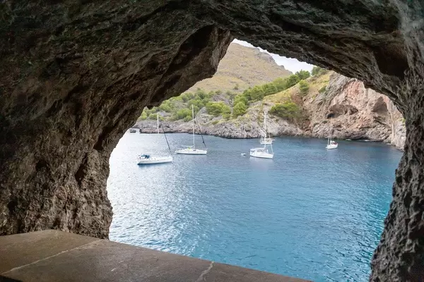 Fünf Segelboote im blauen Wasser in einem Felsenfenster eingerahmt. Sa Calobra, Mallorca