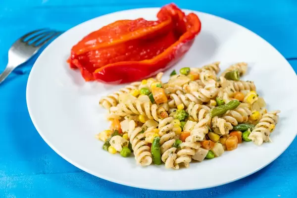 Fusilli-Nudeln mit Gemüse auf einem weißem Teller mit roter Paprika mit Gabel