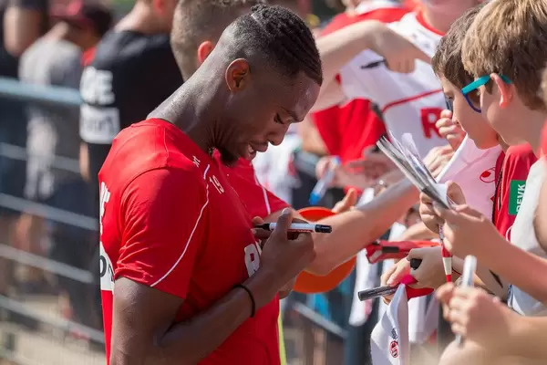 Fußballer Kingsley Ehizibue unterschreibt sein eigenes Trikot und unterhält sich mit jungen Fußballfans und Kindern