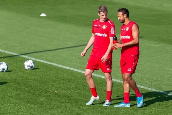 Fußballspieler in roten Trainingstrikots: Lars Bender und Karim Bellarabi unterhalten sich auf dem Fußballfeld, während der Trainingspause
