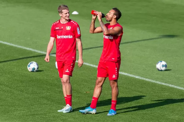 Fußballspieler Karim Bellarabi trinkt aus einer Coca Cola Trinkflasche, neben lachendem Lars Bender