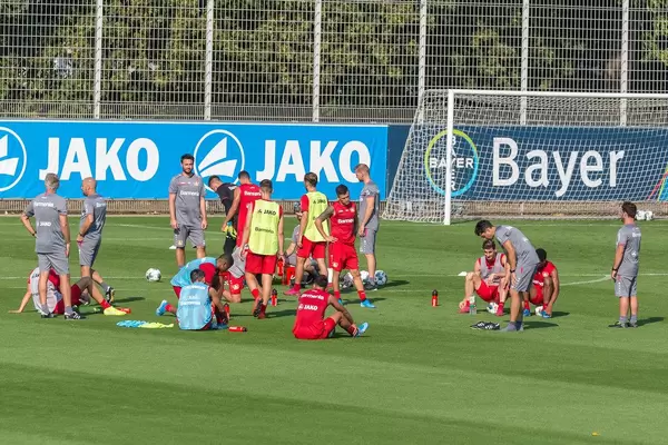 Fußballtrainer und erschöpfte, verschwitzte Fußballspieler sitzen während der Trainingspause auf dem Rasen