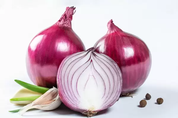 Ganze und halbierte rote Zwiebeln mit Knoblauchzehen und Pfefferkörnern