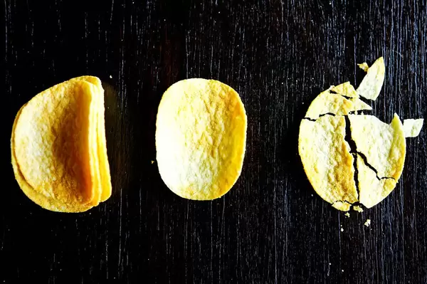 Ganze und zerbrochene Kartoffel-Chips auf schwarzem Hintergrund