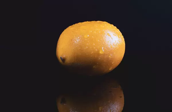 Ganze Zitrone mit Wassertropfen spiegelt sich in schwarzem Hintergrund