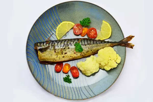 Gebackene Makrele mit Blumenkohl und Kirschtomaten auf einem Teller mit Zitronenscheiben