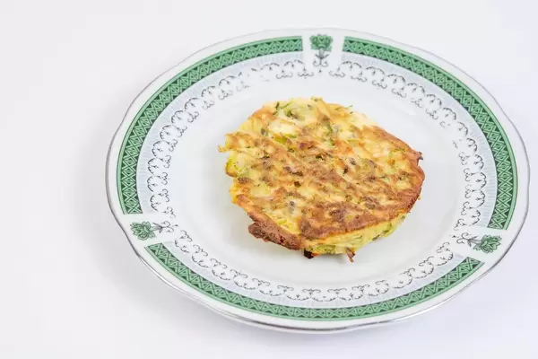 Gebackene Zucchini-Fleisch Küchlein auf grün verziertem Teller vor weißem Hintergrund