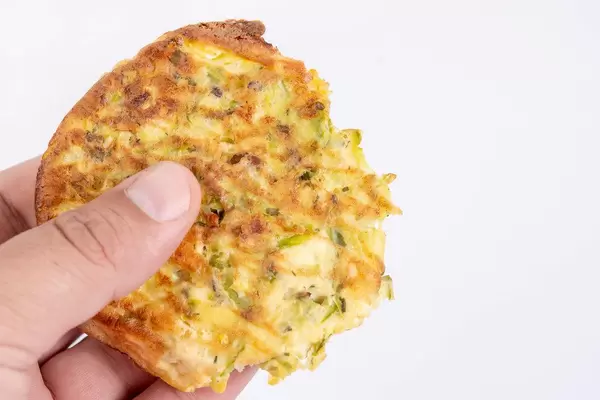 Gebackene Zucchini Fleischbällchen mit Eiern in einer Hand vor weißem Hintergrund
