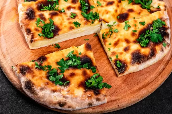 Gebackenes Chatschapuri mit Käse und Kräutern, auf einem runden Küchenbrettchen